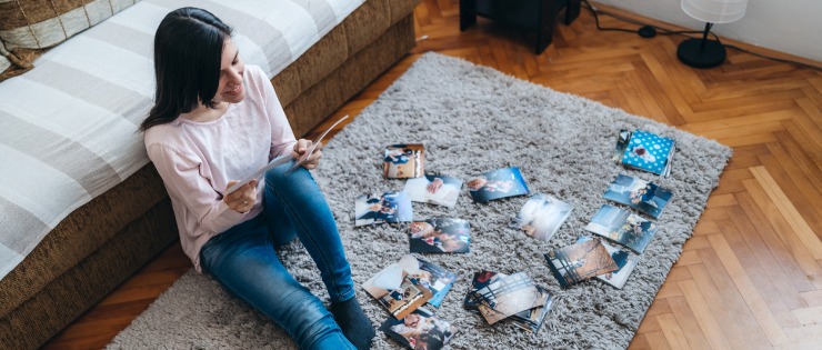 Woman sitting on the floor looking through photos while organising them for a photo book.