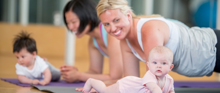 A Mum smiling at her baby while holding a yoga pose at a Mums and bubs yoga class.
