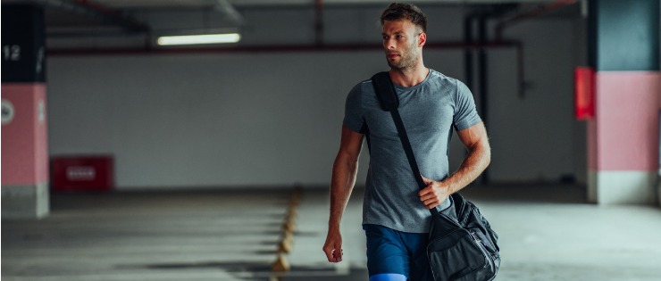 A man carrying a bag of gym clothes and training gear while walking to the gym.
