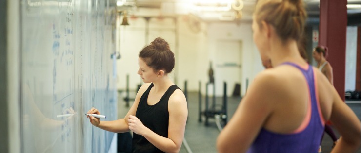 A gym member writing down her training goals with her personal trainer on a whiteboard during her first visit to the gym.