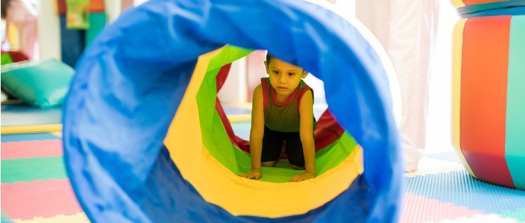 Child crawling through a bright coloured tunnel taking part in occupational therapy. 