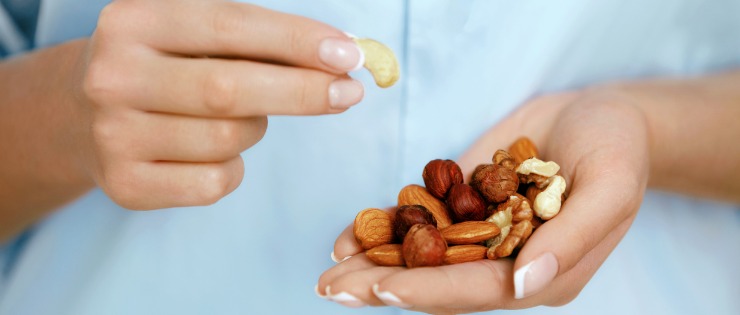 Women in a blue shirt eating nuts as a healthy and high protein snack.