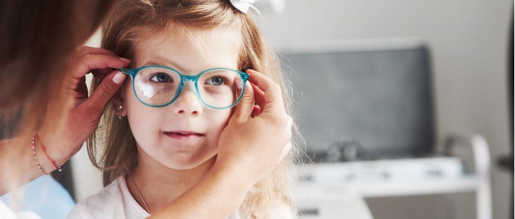 Little girl being fitted with prescription glasses by an optometrist after an eye test.