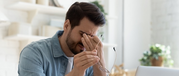 Male office worker suffering from eye strain holding his glasses in hands 