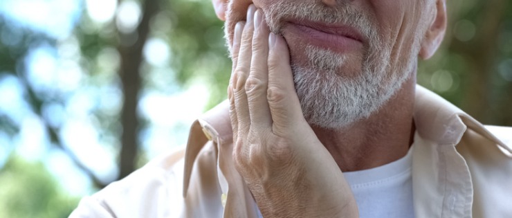 A mature aged man going to the dentist and holding the side of his face in pain due to gum disease. 