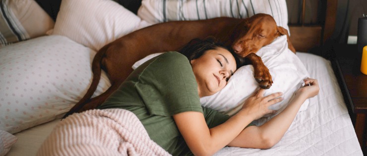 Young woman sleeping with her dog in bed with her.