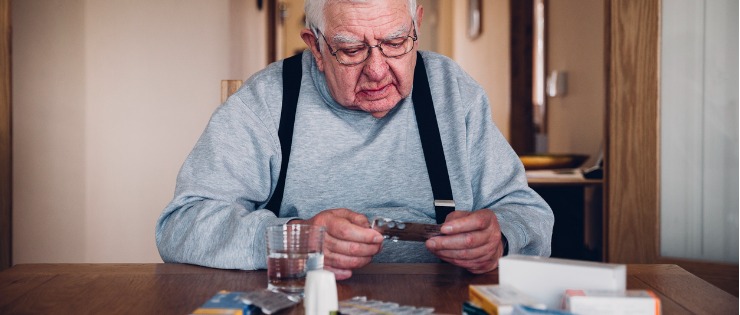 Elderly man looking through his pain medication to relieve his chronic pain at his dining table.
