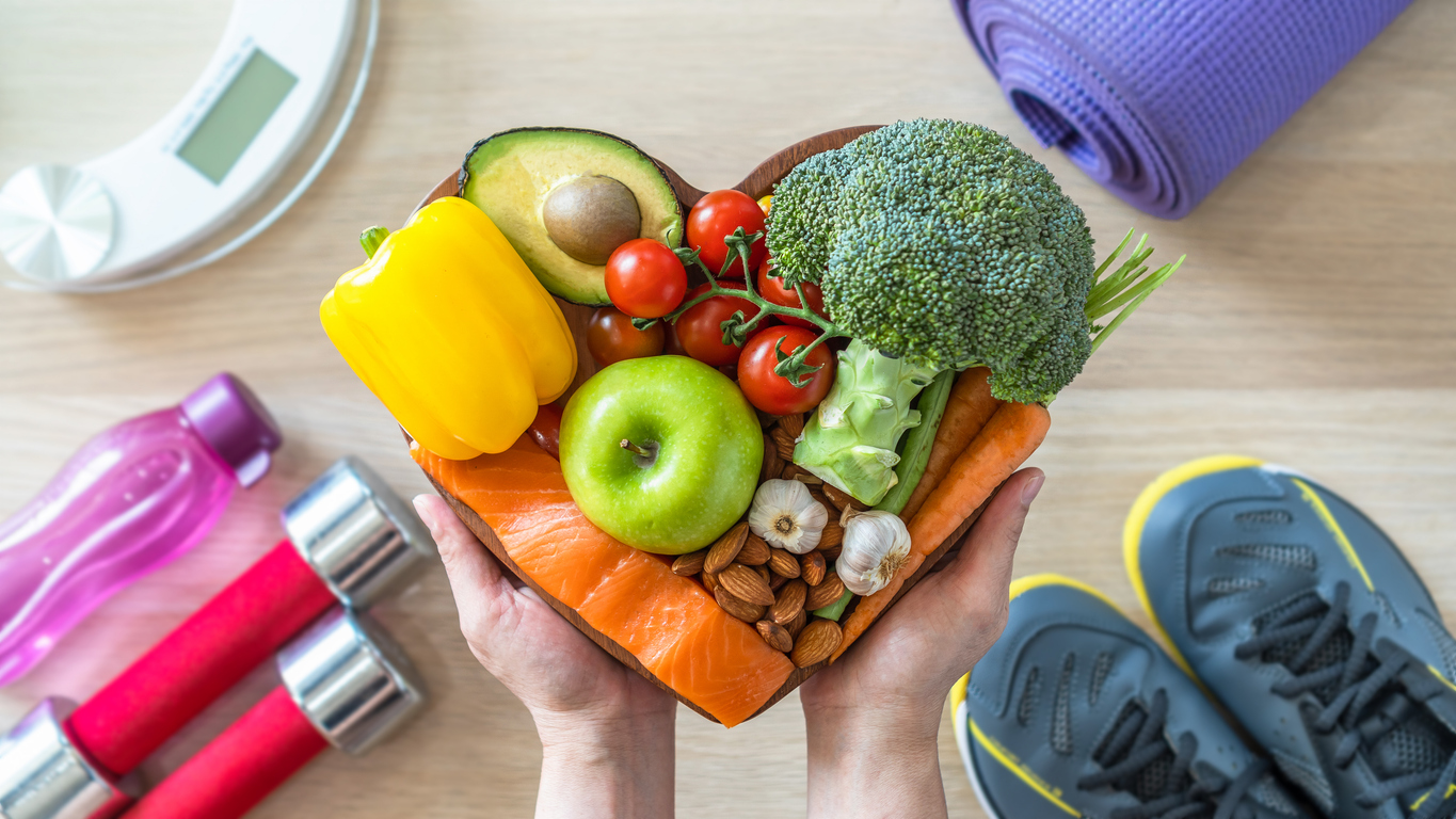 Person holding healthy foods including apple, carrot, and broccoli, exploring weight loss surgery insurances options