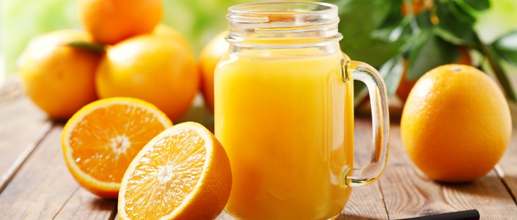 Freshly squeezed orange juice in a mason jar with sliced oranges on a wooden table.