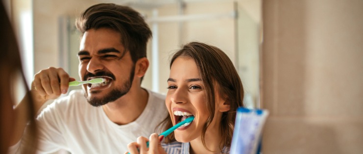 Young couple brushing their teeth in the mirror reducing their chances of gum disease in the near future 