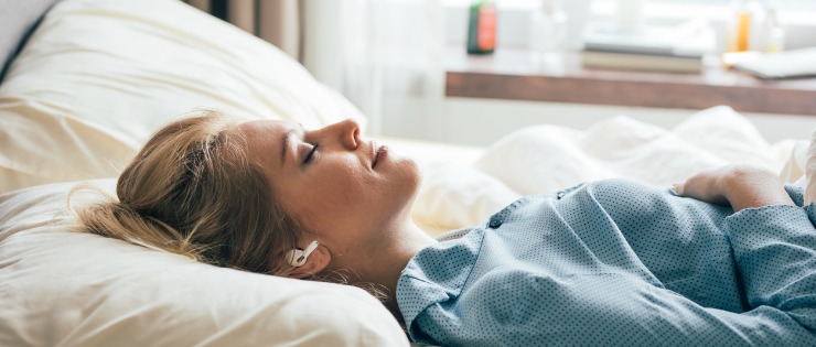 woman laying in bed and listening to music through her wireless earphones 