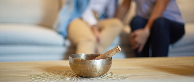 A singing bowl sitting on a table in front of two people speaking about their emotions.