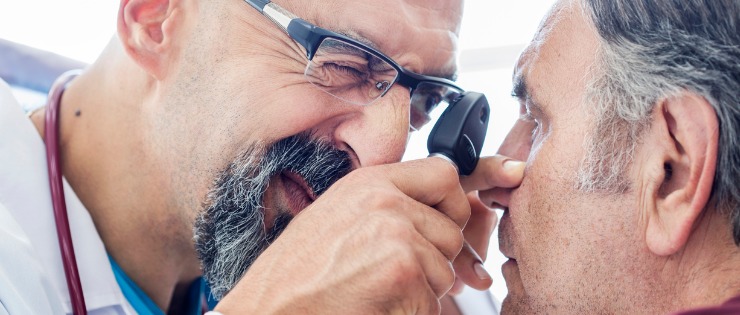 Male optician checking patients eye for early detection of macular degeneration