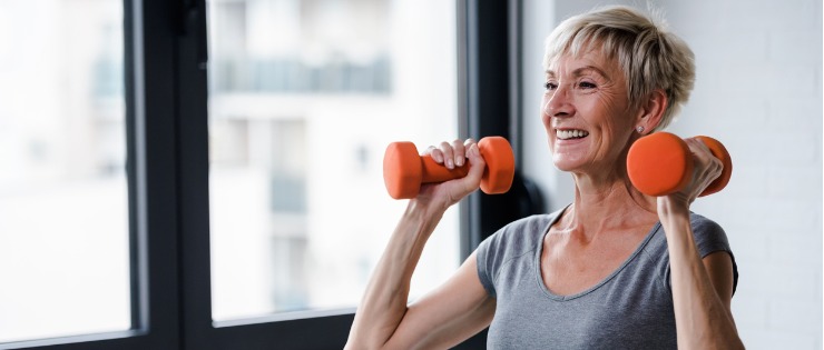 A middle-aged woman strength training by doing an overhead dumbbell press.