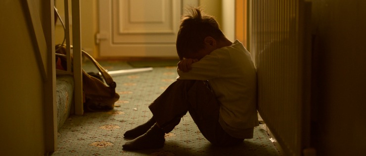 A young boy sitting on the floor and crying after experiencing family violence.