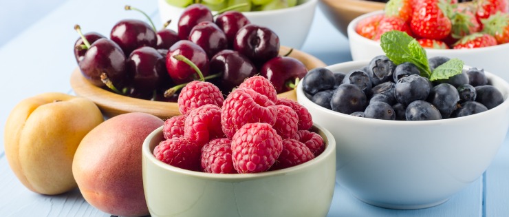 A bench with bowls of fruit on top, including raspberries, blueberries, cherries, grapes, and blackberries. 