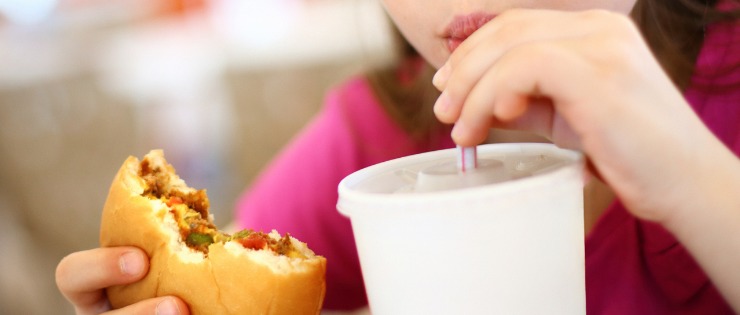 A young girl consuming fast food and a milkshake 