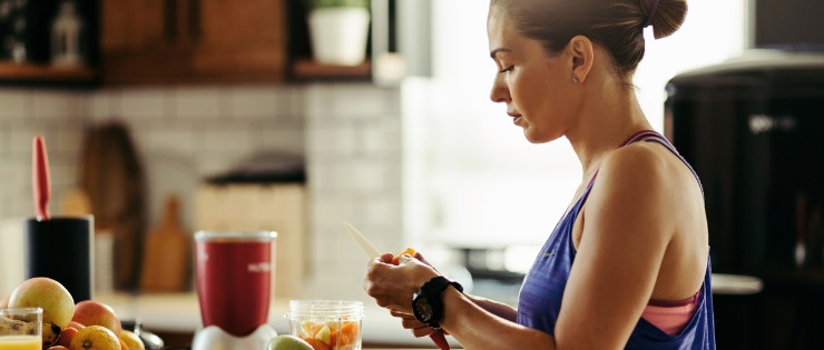 Female making a healthy breakfast smoothie with fruit and vegetables in workout clothing