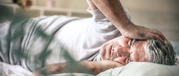 Elderly man lying in bed with depression because he's suffering from chronic pain.
