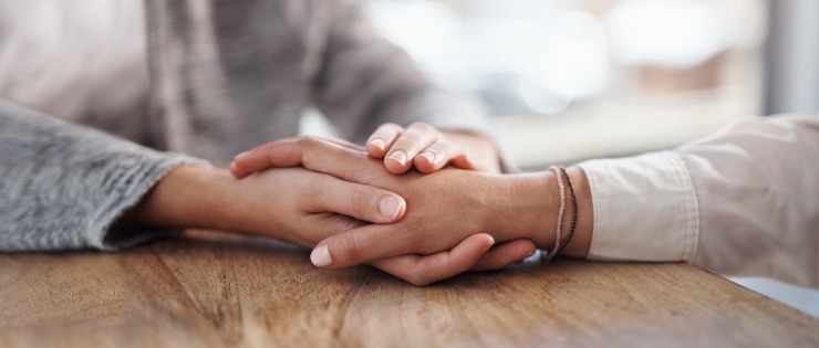 Two people holding hands across a table, talking about emotions and showing empathy for each other.