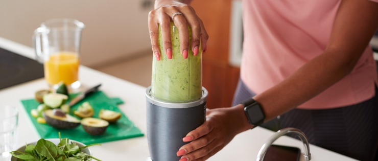 Woman with a wearable fitness tracker prepares a green smoothie to start her day.