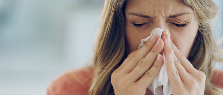 Young woman blowing her nose into a tissue, suffering from the flu. 