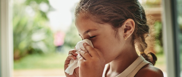Young girl blowing her nose due to an allergic reaction.