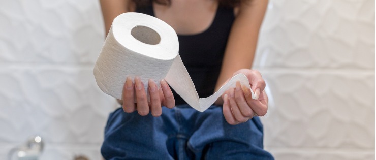 Young female seated on a toilet holding toilet paper suffering from bowel issues