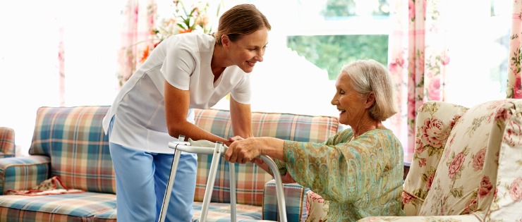 A nurse helping a senior woman do hip strengthening exercises from her couch.