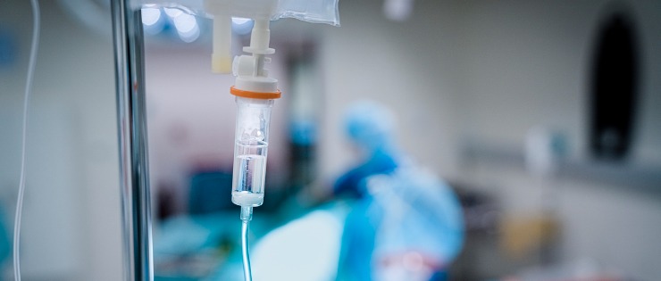 An IV bag hanging up in a COVID-19 ward in the hospital, in the background is a patient who was admitted after receiving a positive result from a rapid antigen test.
