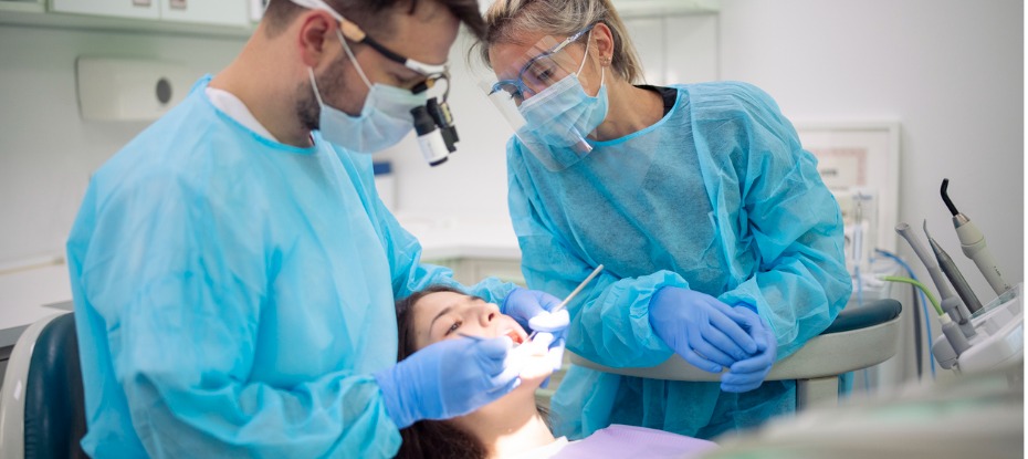 dentist and dental assistance cleaning a woman’s teeth 