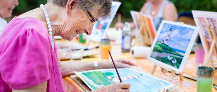 Senior woman painting a picture at a social club, so she can stay mentally active.