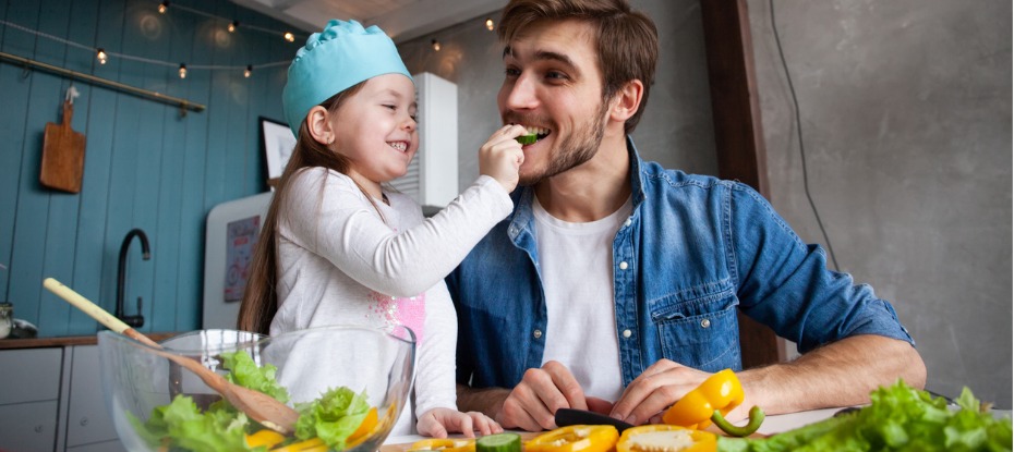 young man with his daughter cooking and eating the rainbow in fruits and vegetables