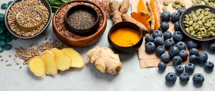 Selection of various superfoods and superfood powders including ginger, turmeric, flaxseeds, chia seeds, blueberries, pumpkin seeds, goji berries, and almonds.