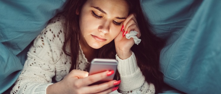 Girl hiding under covers sad about rude text messages.
