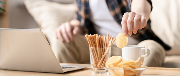 Young man working from home reach for a bowl of snacks to eat while being bored 