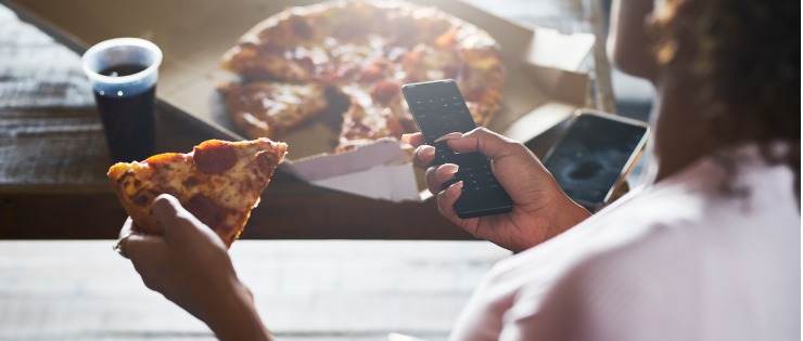 Young woman stress eating pizza while scrolling on her phone