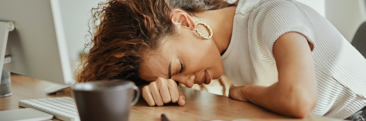 woman with her head on the desk and eyes closed, looking burnt out