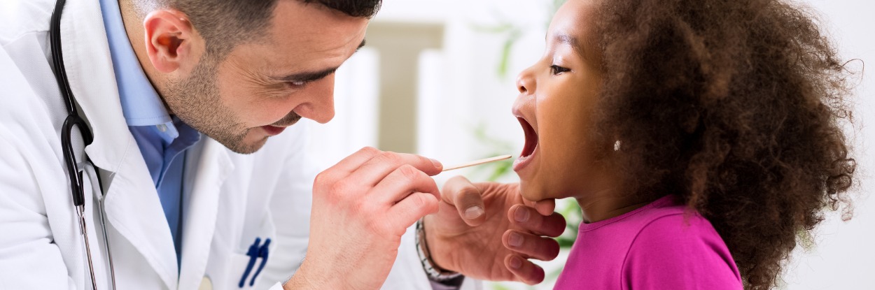male doctor examining young girl’s throat with a tongue depressor stick