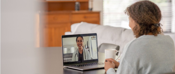 Woman sitting and talking to a doctor on her computer via a telehealth video conferencing appointment