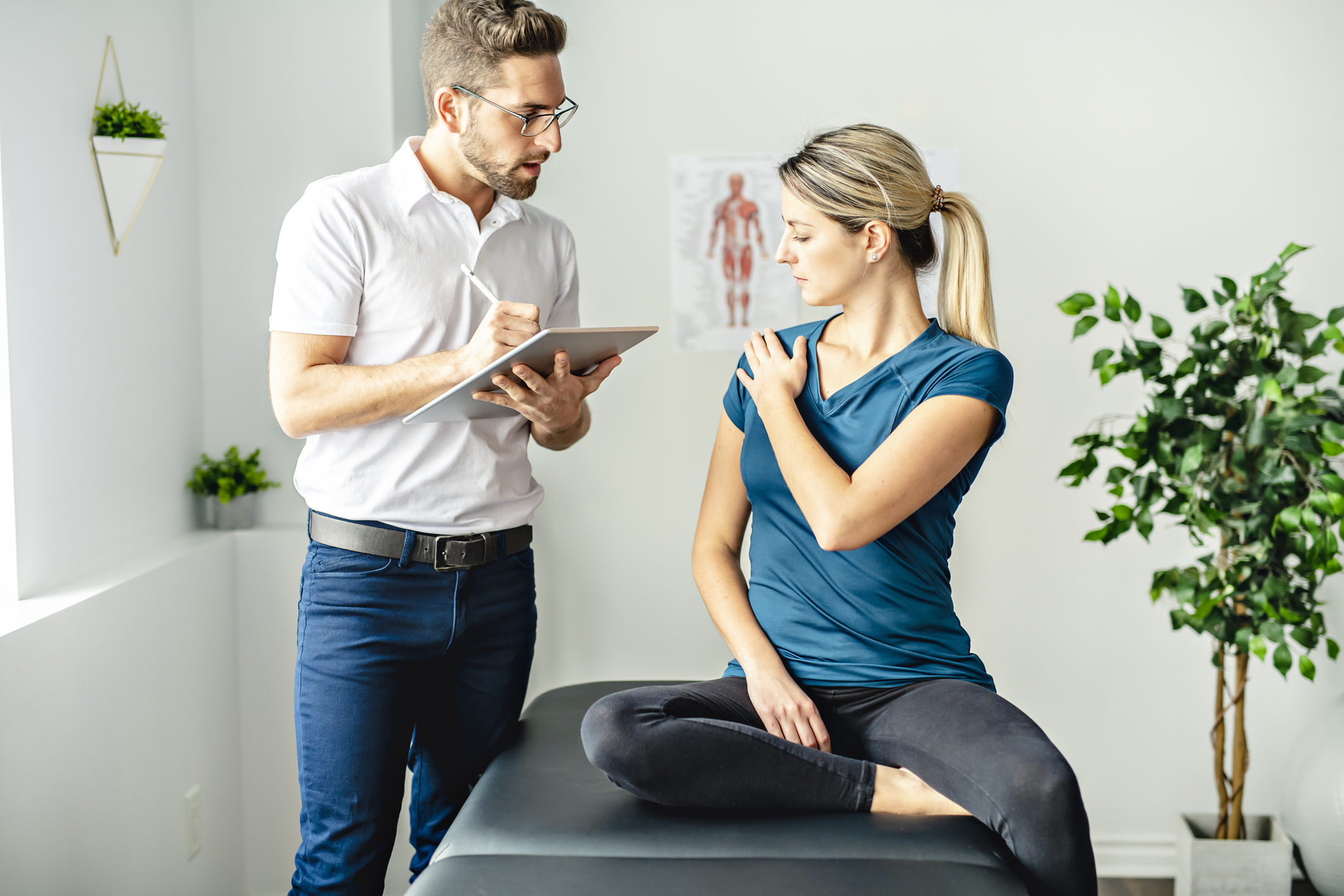 Lady sitting on consulting bench talking to a doctor while holding her shoulder