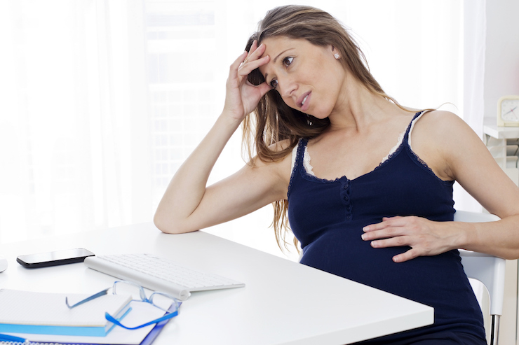 a stressed pregnant woman sat at her desk with hand on head