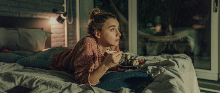 young female binge watching tv at night while eating